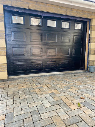 A black garage door with rectangular panels and small windows at the top