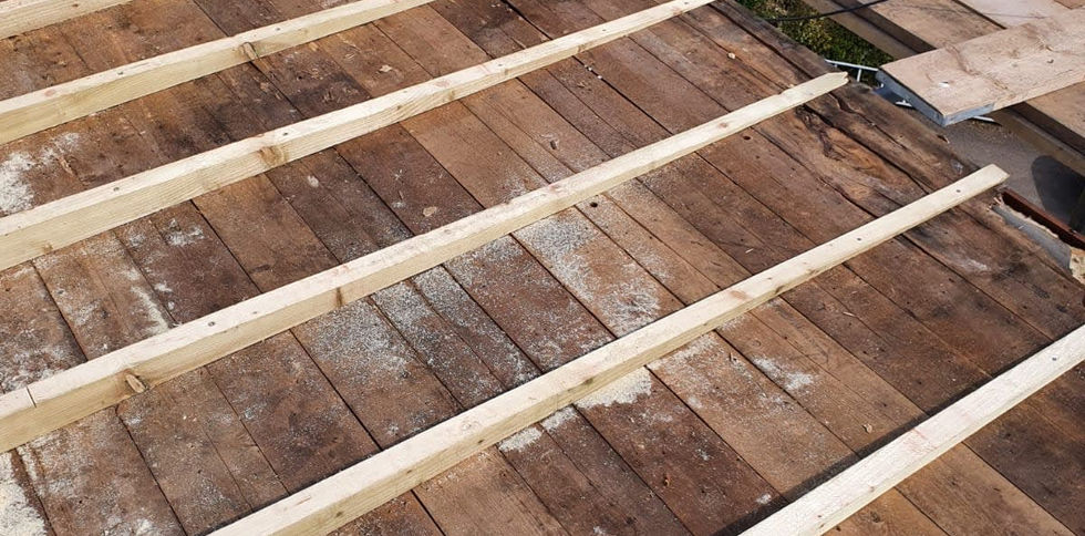 A partially stripped roof showing wooden beams laid over exposed boards