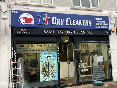Exterior of TT Dry Cleaners featuring a prominent sign, service listings, and a display of cleaned clothes in the window