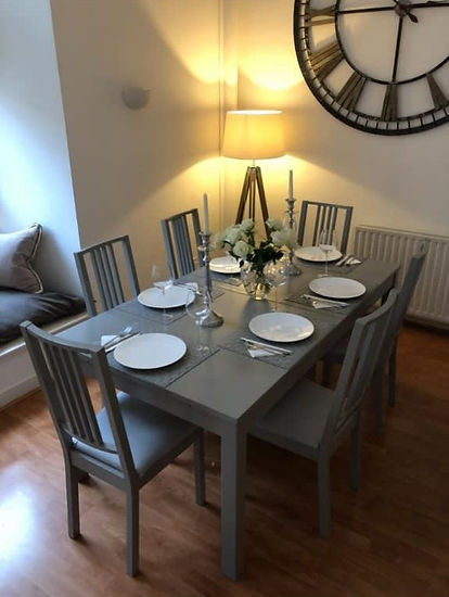 A grey dining table set for six, featuring white plates and glassware