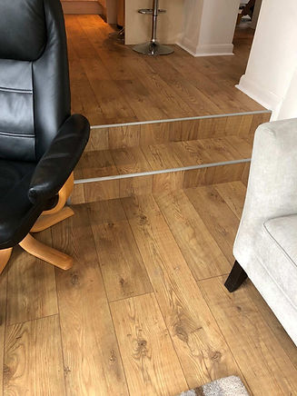 Interior room corner with wooden flooring, part of a black chair, and a silver bar stool