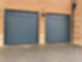 Two closed, dark gray rolling garage doors set in a red brick exterior