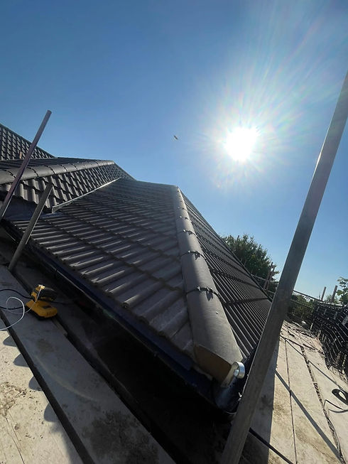 A sloped rooftop with tile shingles under a clear blue sky, sunlight reflecting off the surface, and a distant flying object