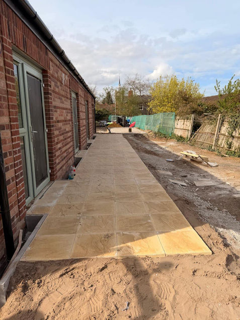 A newly tiled pathway with beige tiles runs alongside a brick building