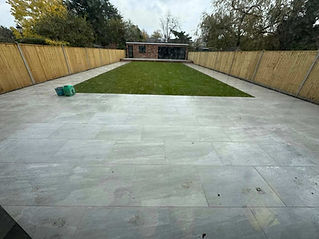 A wide white patio featuring grass and enclosed by a fence