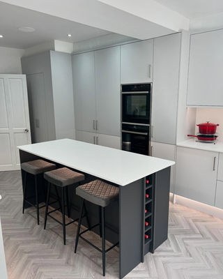 Modern kitchen featuring sleek gray cabinetry, a white island with three upholstered stools, and a wine storage compartment