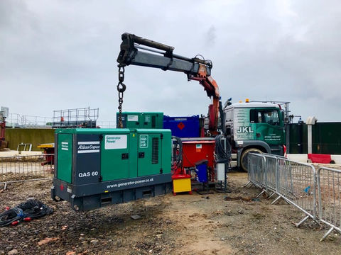 A crane lifting a large green machine at a construction site.