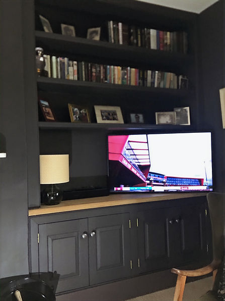 Dark built-in shelving unit with books, framed photos, and a TV