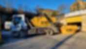 A truck from BN Skips parked outside a warehouse with two yellow skips