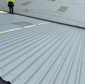 A worker in a high-visibility jacket inspects a corrugated metal rooftop
