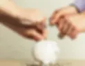 Three hands place coins in a white piggy bank