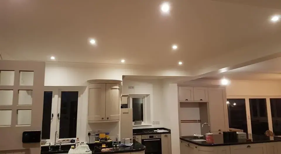 Spacious kitchen with white cabinets, black countertops, and a wooden floor, illuminated by recessed ceiling lights