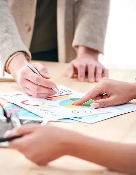 The hands of three people are pointing at colourful charts on a table