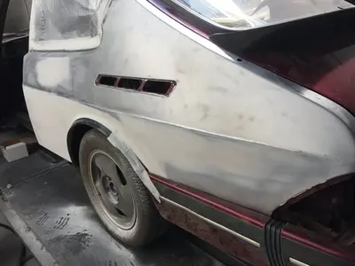 Partially restored vintage car with a mix of white primer and maroon paint