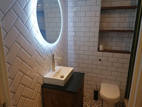A modern compact bathroom design showcasing a glowing backlit mirror over a vanity unit setup
