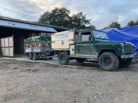 A green Downing Logs truck with a caged trailer loaded with firewood