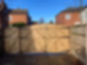 Wooden double gate in a fence, with houses in the background under a clear sky