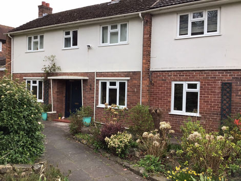 A daytime shot of a clean, white-rendered home exterior with red brick base styling