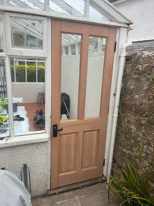 A wooden half-glazed door with a black handle, set in a white wall next to a conservatory