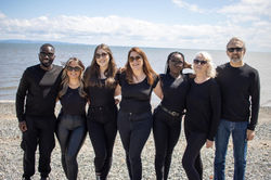 A group of six people dressed in black, standing together on a beach
