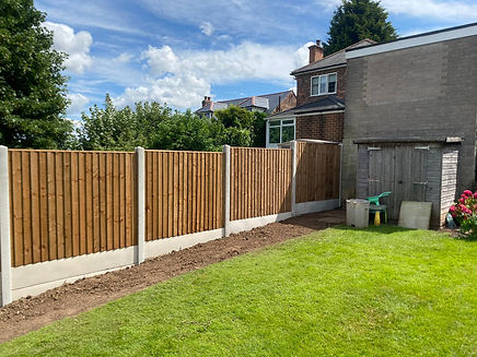 A new wooden fence with concrete posts alongside a lush green lawn near a brick house