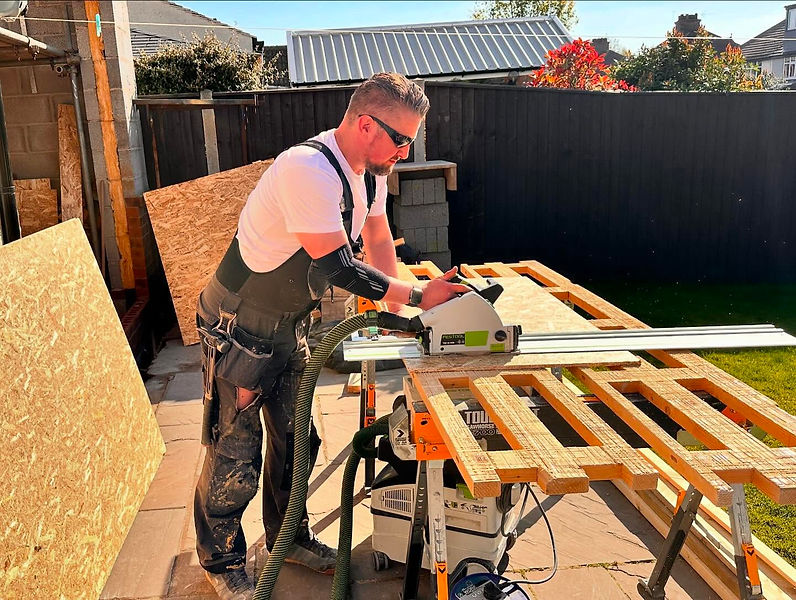 A joinery professional with tool belt using a circular saw to precisely cut timber planks on a workbench