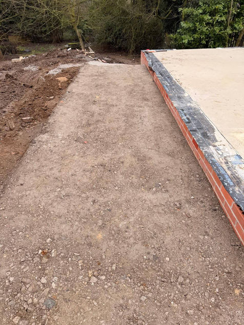 A freshly laid gravel path leads to a concrete slab foundation bordered with red bricks