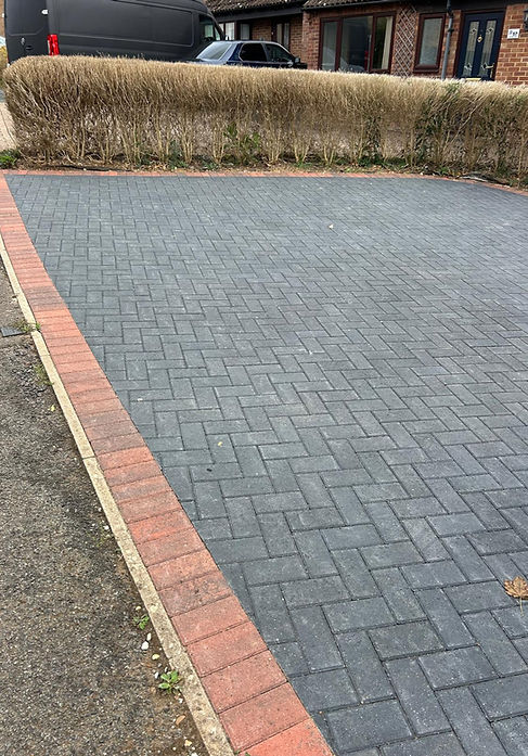 A clean, empty driveway with grey interlocking brick pavers bordered by a red brick edge