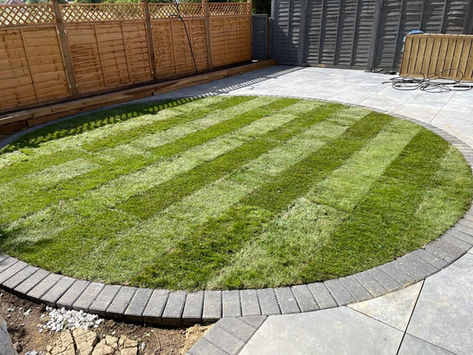 Circular lawn with alternating light and dark green stripes, bordered by grey bricks
