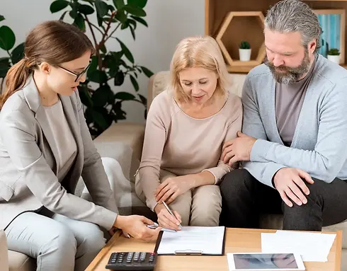 A woman in a suit guides a couple signing documents at a table