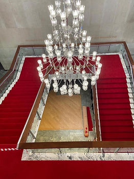 A luxurious staircase with bright red carpet beneath a large chandelier