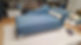 A stylish blue chaise lounge with a curved backrest and decorative pillow, set against a backdrop of tools and shelving in a workshop