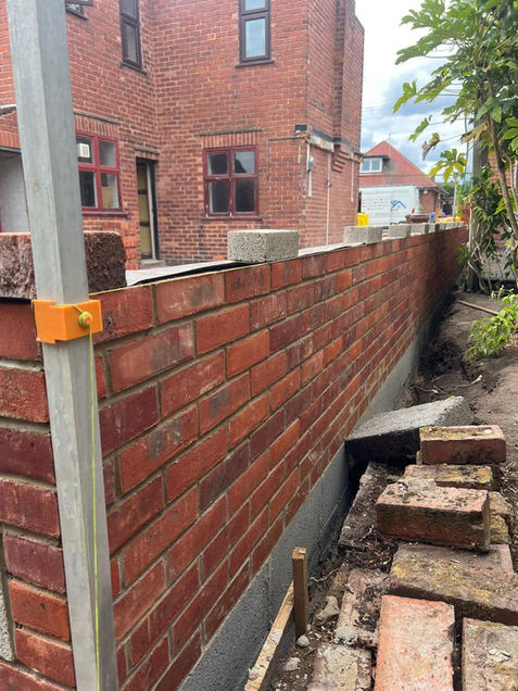 A newly constructed red brick wall in front of a brick building