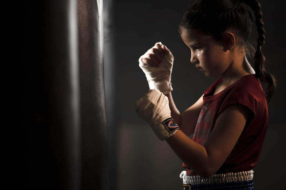 A young girl in a red shirt and white boxing hand wraps stands focused