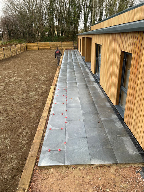 Newly laid slate tiles on a walkway beside a building with wooden facade, person in distance