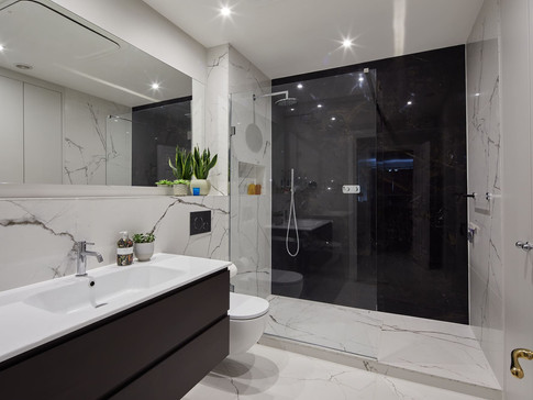 Modern bathroom with white marble walls, a large mirror, and a sleek sink