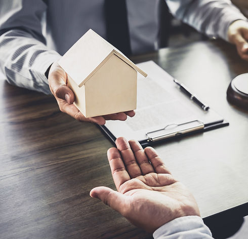 Two people exchange a small wooden house model over a desk
