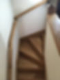 A narrow, winding wooden staircase with triangular steps and a smooth wooden railing