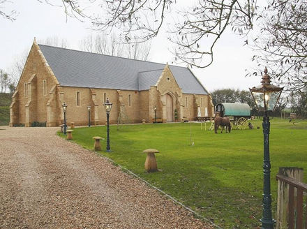 A traditional stone church with a horse-drawn carriage on a grassy lawn, flanked by lampposts and a gravel path