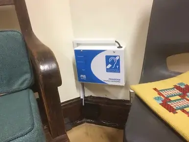 Blue hearing assistance device mounted on a wall near wooden and plastic chairs