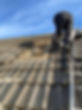 A worker with a ladder, repairing a roof with several tiles removed