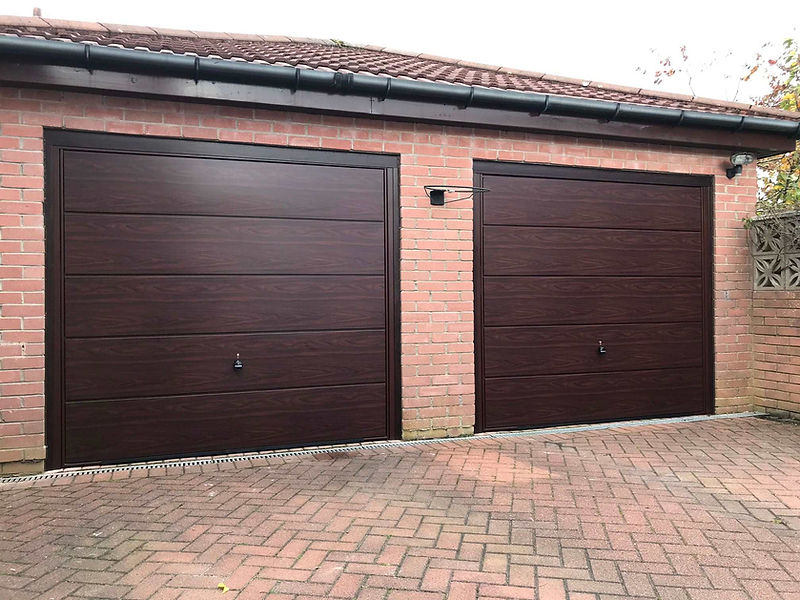 Two closed garage doors are set in a brick wall, featuring dark brown wood panelling with black handles