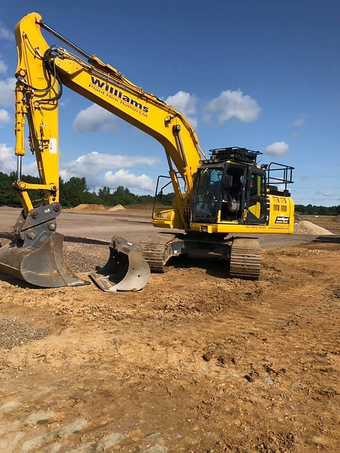 Yellow tracked excavator parked on a dirt construction site against a blue sky