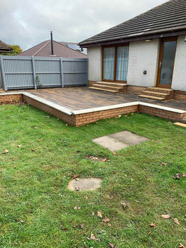A patio area with gray fencing, brick steps, and a grassy yard covered in leaves, adjacent to a house with a slanted roof