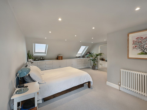 A cosy attic bedroom featuring a white bed, skylights, and a sleek dresser