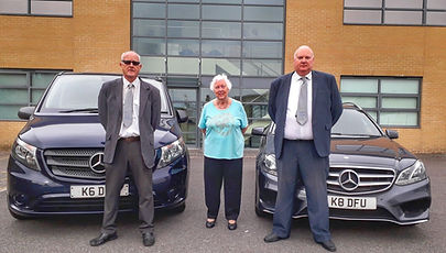 Two Mercedes in the background and two men and a woman is standing in foreground