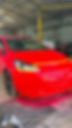 A bright red car with black wheels is parked in a garage, partially masked with yellow tape for painting