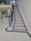 A grand white staircase with black railings, featuring plush cream carpeting, leading to an open, light-filled foyer