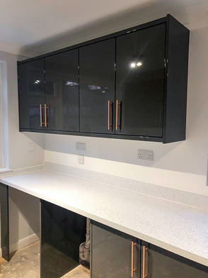 Modern kitchen with sleek, reflective black cabinets featuring rose gold handles, and a smooth, white countertop