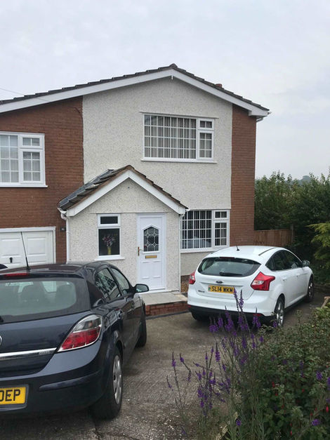 A white residential house front with a parked car sitting in the brick driveway